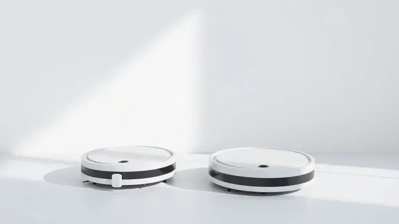 Comparativo visual entre dois modelos genéricos de robôs aspiradores em um ambiente de estúdio minimalista.